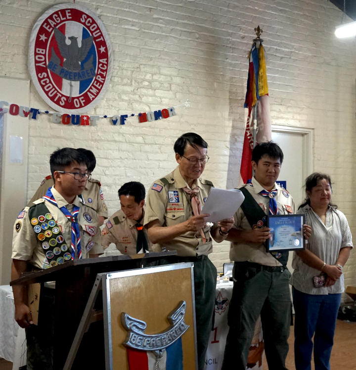 Troop chairman reads a speech from a collection of papers he is holding. To the right and left are two new eagle scouts.