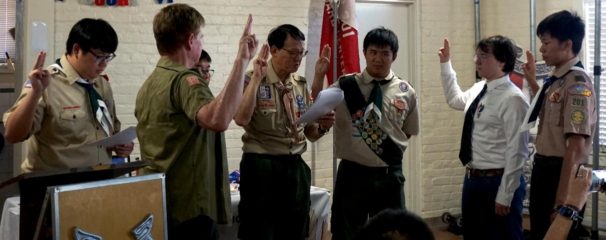 Several eagle scouts stand in a circle, holding up scout signs and reciting something