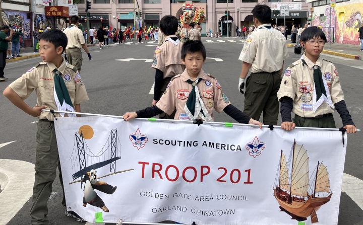 Three scouts hold the troop 201 banner in front of a dragon