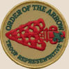 Order of the Arrow troop representative badge: A red arrow pointing left, a small green trefoil on the right, the words order of the arrow curved near the top semicircle, and the words troop representative curved near the bottom semicircle