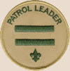 Patrol leader badge: two horizontal green lines with a small trefoil below them and the words patrol leader curved near the edge of the top semicircle